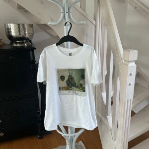 Kendrick Lamar vit t-shirt med tryck - Vit t-shirt med stort tryck av Kendrick Lamars album 'Good Kid, M.A.A.D City' både fram och bak. Framsidan har ett foto och baksidan har text, bilder och albumdetaljer. Rund hals och korta ärmar, tillverkad i mjuk bomull. Perfekt för dig som gillar hiphop och streetwear.