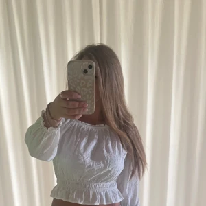 Vit  blus från Kappahl - Superfin vit blus från Kappahl med offshoulder-modell och långa puffiga ärmar. Toppen är croppad med volangkant nertill och har resår vid axlar och midja för en snygg passform. Perfekt till jeans eller kjol för en fräsch look.