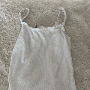 Vit ribbad linnetopp med spets - Supersöt vit linnetopp med tunna axelband och spetsdetaljer längs kanterna. 🥰
