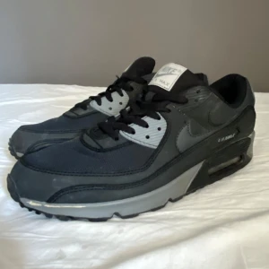 Nike Air Max 90 - Ett par Air Max 90s i svart grå färg som jag köpte helt nya i vintras jag har använt dom lite men inte så mycket men det finns lite skavanker då färgen har lossnat lite på sidorna men inget man tänker på. Det är storlek 44,5 men jag har 42-43 och dom passar prima. Pris går att diskutera!