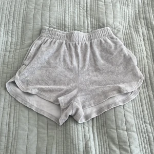Gråa mjukisshorts från Gina Tricot - Gråa shorts från Gina i handduksmaterial. Nästan oanvända och väldigt bekväma! OBS! På sista bilden är shortsen nedvikta ett varv! 