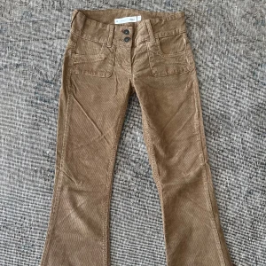 Bruna bootcut manchesterbyxor Subdued - Snygga bruna manchesterbyxor från Subdued i bootcut-modell med låg midja. Byxorna har två framfickor, två bakfickor och dubbla knappar i midjan. Perfekt för dig som gillar retrovibbar och vill sticka ut med coola detaljer och skön passform.