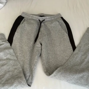 Grå mjukisbyxor från SOC med svarta detaljer - Grå mjukisbyxor från SOC med svarta paneler längs sidorna och snörning i midjan. Byxorna har en bakficka och är tillverkade i mjukt material som passar perfekt för chill eller träning. Klassisk och enkel design med bekväm passform.