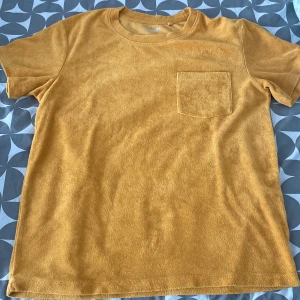 Gul frotté t-shirt från Kappahl - Schysst gul t-shirt från Kappahl i frottématerial. Modellen har rund hals, korta ärmar och en bröstficka, använd 2-3 gånger samt väldigt sparsamt. Hojta till vid övriga funderingar 👍