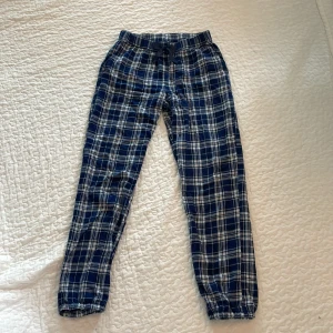 Rutiga mjukisbyxor från Kappahl - Blå och vita rutiga mjukisbyxor från Kappahl i storlek 158/164. Byxorna har resår och snörning i midjan med en söt rosett framtill samt resår vid bensluten. Perfekta för chill dagar hemma.