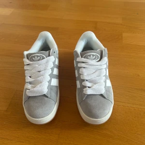 Adidas Campus 00s Grå - Säljer ett par Adidas Campus 00s i grå/vit färg, storlek 38. Endast använda 1 gång, i nyskick utan några skador eller fläckar. Normala i storleken och passar perfekt till sommar och höstväder. Skolåda finns men är lite skadad. Nypris ca 1 400 kr.