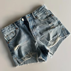Blå jeansshorts  - Snygga ljusblå jeansshorts från New Yorker i storlek S. De har slitna detaljer, fransig nederkant och klassisk femficksmodell. Perfekta för sommardagar när du vill ha en avslappnad och trendig look!