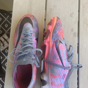 Nike Mercurial Zoom fotbollsskor grå/rosa - Säljer ett par Nike Mercurial Zoom fotbollsskor i grått och rosa med svarta detaljer. Skorna har stickad ovandel, snörning och en cool mönstrad design. Yttersulan är rosa med dobbar för bra grepp på planen. Perfekta för dig som vill sticka ut på matchen!