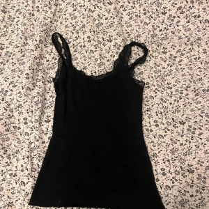 Svart spetskantad linnetopp Esmara - Svart ribbad linnetopp från Esmara med smala axelband och fina spetsdetaljer längs urringningen. Toppen är figurnära och har en klassisk, enkel look som passar till många olika stilar. Tillverkad i mjuk bomullsmix för extra komfort.