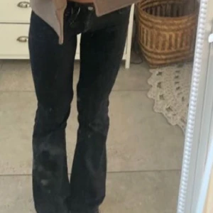 Svarta bootcut jeans W26 L32 - Snygga svarta bootcut jeans med klassisk femficksdesign och låg midja. Jeansen har en stilren look med raka ben som blir vidare nedtill. Materialet är jeans i bomull med lite stretch för extra komfort. Perfekta för dig som gillar en tidlös och cool stil.