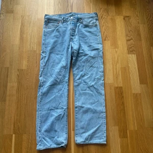 Levi's 501 ljusblå jeans W33 L32 - Klassiska Levi's 501 jeans i ljusblå denim. Rak passform med fem fickor och knappgylf. Snygg vintagekänsla och ikonisk läderpatch bak i midjan. Perfekta för dig som gillar tidlös stil och vill ha ett par riktigt schyssta jeans. Aldrig använda så nyskick!