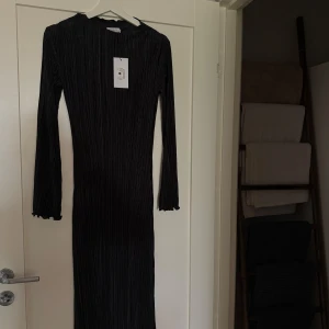 Svart plisserad långklänning Stockh LM - Supersnygg svart långklänning från Stockh LM Studio i plisserat tyg. Klänningen har långa ärmar med vågig kant och en smal, figurnära passform. Perfekt för dig som gillar stilrena och trendiga plagg med cool struktur. Väldigt stretchig. Kan mötas på Ekerö annars står köparen för frakt. 