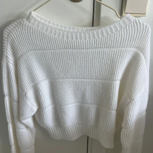 Vit ribbad stickad tröja - Säljer en vit stickad tröja med ribbad struktur och rund hals. Tröjan har långärmade och är lite croppad i modellen, vilket ger en modern och chill vibe. Perfekt att matcha med jeans eller kjol för en enkel och snygg look.