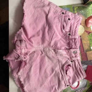 Rosa jeansshorts från Zara - Säljer ett par ljusrosa jeansshorts från Zara med fransiga kanter och klassisk femficksdesign. Shortsen har normal passform och är perfekta för varma sommardagar. Snyggt slitna detaljer och mjukt bomullsmaterial gör dem både bekväma och trendiga.