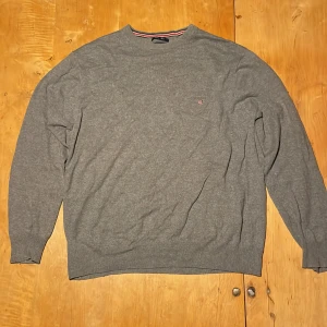 Grå GANT tröja i bomull och ull - Snygg grå tröja från GANT i en mix av bomull och ull. Klassisk rund halsringning med diskret GANT-logo på bröstet och ribbade muddar. Perfekt för dig som gillar stilren och enkel design med en soft känsla.