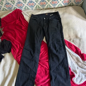 Svarta jeans från Lee - Säljer ett par svarta jeans från Lee med klassisk femficksdesign och raka ben. Jeansen har Lee-logga på knapp och etikett i midjan. Snygg, enkel stil som funkar till det mesta. Materialet är jeans i bomull.