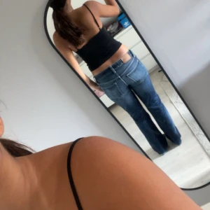  blå jeans bootcut - Säljer ett par klassiska jeans i blå denim med snyggt slitna detaljer. Modellen har låg midja, med lätt bootcut och knäppning med knappar. Perfekta för dig som gillar vintagevibbar och tidlös stil.