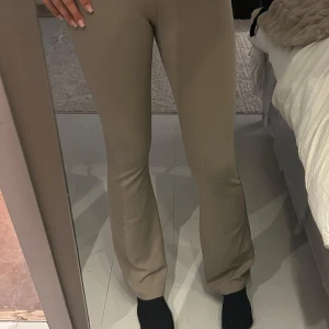 Beiga bootcut byxor med stretch - Säljer ett par snygga beiga bootcut byxor med skön stretch och figurnära passform upptill. Byxorna har en klassisk look med utsvängda ben och passar perfekt till sneakers eller boots. Superbekväma och lätta att styla till olika outfits.
