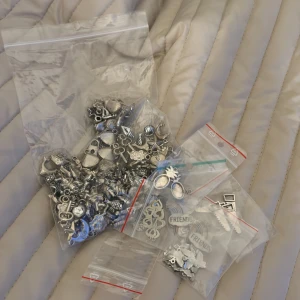 Stort paket med silverfärgade berlocker - Säljer ett stort paket med blandade berlocker i silverfärg, perfekta för att göra egna armband, halsband eller örhängen. Innehåller motiv som nycklar, hjärtan, stjärnor, månar, ananas, regnbågar med texten 'FRIENDS', planetberlocker med glittriga stenar och andra coola former. Materialet är metall.