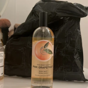 The Body Shop Pink Grapefruit Body Mist - Fräsch body mist från The Body Shop med doft av pink grapefruit. Kommer i en genomskinlig glasflaska med svart spraykork och en färgglad etikett med grapefruktmotiv. Innehåller 100 ml och ger en lätt, fruktig känsla.