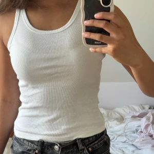 Vit ribbad linnetopp från Weekday - Säljer en klassisk vit ribbad linnetopp från Weekday. Modellen är ärmlös med rund halsringning och tight passform. Perfekt att styla med jeans eller kjol för en clean och enkel look. Materialet är mjuk bomull som känns skönt mot huden.