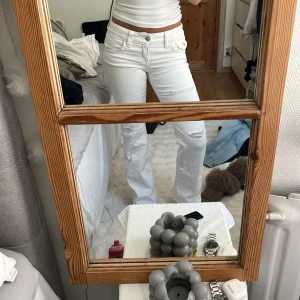 Vita jeans med slitningar och utsvängda ben - Säljer ett par vita jeans med snygga slitningar på knäna och utsvängda ben. Byxorna har låg midja, klassiska fem fickor och coola detaljer som knappstängning och bakfickor med knapp. Klicka gärna på ”köp nu”!