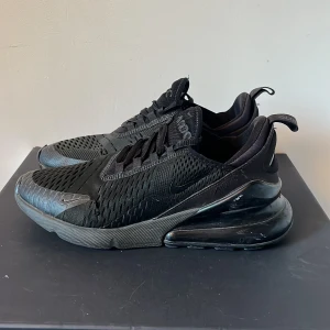 Svarta Nike Air Max 270 sneakers - Svarta Nike Air Max 270 sneakers med mesh-ovandel och stora luftbubblor i sulan. Snygg sportig look med diskreta detaljer och snörning. Perfekta för dig som gillar streetstyle och vill ha bekväma skor med modern vibe.