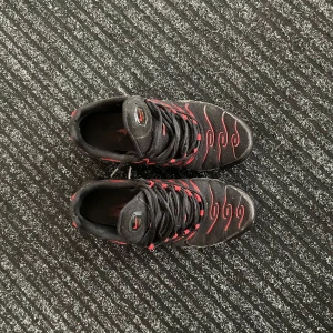 Nike Air Max Plus Tn Svart/Röd - Nike Air Max Plus Tn sneakers i svart mesh med röda detaljer och vågiga linjer. Snygg design med synlig Air Max-dämpning i sulan och Tn Air-logga bak. Skorna har snörning och en sportig vibe som sticker ut. Storlek 42,5. Köpta för 1899kr säljer för 749kr priset kan diskuteras vid snabb affär 