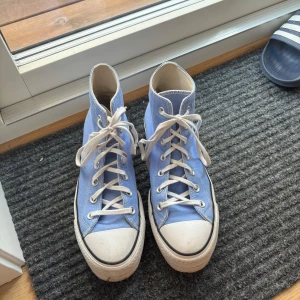 Blå Converse Chuck Taylor All Star - Säljer ett par klassiska Converse Chuck Taylor All Star high-tops i ljusblå canvas med vita snören och gummisula. Skorna har rund tå, vita detaljer och den ikoniska loggan på sidan. Perfekta för dig som vill ha en tidlös och cool stil. Nästintill oanvända. Köpta för 800-1200kr. Pris kan diskuteras.