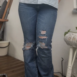 Blå slitna bootcut jeans - Säljer ett par blå jeans med lågmidja och slitningar / hål över knäna. Tillverkade i strechigt jeanstyg som är väldigt mjukt. Kontakta mig för fler bilder om ni vill! 💓💞