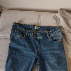 Blå bootcut jeans från 157 - Snygga blå jeans från 157 med klassisk femficksdesign och dubbla knappar i midjan. Jeansen har bootcut-ben och normal passform, perfekta för en avslappnad stil. Tillverkade i jeansmaterial med ljusblå tvätt och raka bakfickor.