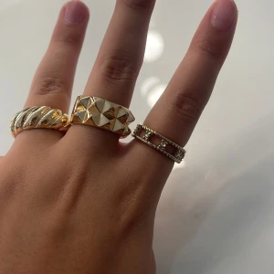 Tre snygga guldringar med olika design - Säljer tre guldfärgade ringar: en med snurrad design, en bred med pyramidformade detaljer och en tunnare med små pärlor och öppna rutor. Perfekt för dig som gillar att mixa och matcha olika stilar på fingrarna.Du köper ring för sig 