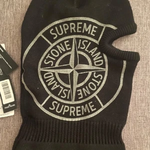 Svart balaclava från Stone Island x Supreme - Säljer en svart balaclava med stort broderat Stone Island x Supreme-logo framtill. Masken har ett öppet parti för ögonen och är ribbstickad nedtill. Loggan lyser i mörkret och materialet är mjukt och stretchigt.