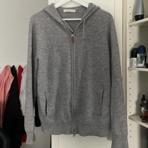 Grå hoodie i kashmir från Sayless - Mjuk och lyxig grå hoodie från Sayless i 100% kashmir. Tröjan har dragkedja framtill, två fickor och huva. Perfekt för en avslappnad och stilren look.