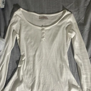 Vit ribbad långärmad topp från Anna Field - Säljer en vit långärmad topp från Anna Field med ribbad struktur och rund halsringning. Toppen har tre dekorativa knappar framtill och är i ett mjukt, stretchigt material. Perfekt att styla till jeans eller annat.