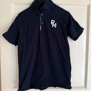 Mörkblå pikétröja från Race Marine - Säljer en mörkblå pikétröja från Race Marine med broderad RM-logga på bröstet. Tröjan har korta ärmar, klassisk krage och knappar framtill. Perfekt för en sportig och stilren look.