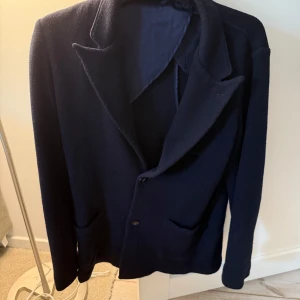 Mörkblå kavaj - Säljer en stilren mörkblå kavaj med klassisk krage och två knappar framtill från John Henric. Kavajen har två fickor och är helfodrad på insidan. Perfekt för dig som vill ha en enkel och snygg look.