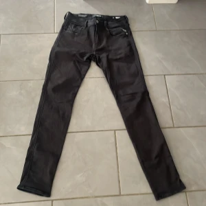 Svarta Replay Anbass jeans w30 L32 - Säljer ett par svarta Replay Anbass jeans med klassisk femficksdesign och smal passform. Byxorna har dragkedjegylf och Replay-logga på bakfickan. Perfekta för dig som gillar stilrena och bekväma jeans.