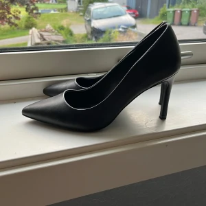 Svarta pumps - Klassiska svarta pumps med spetsig tå och hög klack från Gina Tricot. Skorna är i syntetmaterial och har en elegant och tidlös design som passar till många olika tillfällen. Endast använda en gång💕
