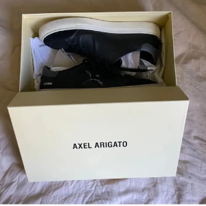 Svarta Axel Arigato Clean 90 Triple B Bird sneakers - Säljer ett par svarta Axel Arigato Clean 90 Triple B Bird sneakers med vit sula och grå detaljer. Skorna har snörning och en stjärndetalj på sidan. Perfekta för dig som gillar stilrena och trendiga sneakers.