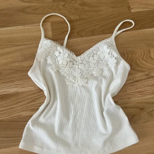 Vit ribbad linnetopp med spets - Supersöt vit ribbad linnetopp från miss Selfridges med smala axelband och vacker spets med blommönster längs ringningen. Perfekt att styla till jeans eller kjol för en fräsch look.