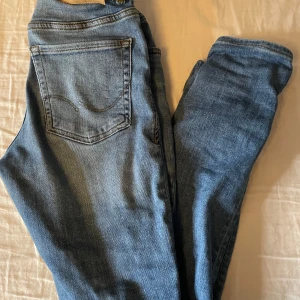 Blå jeans från Jack & Jones - Klassiska blå jeans från Jack & Jones med fem fickor och normal passform. Jeansen har en knappgylf och tydliga sömmar, tillverkade i bomull med en lätt tvättad look. Perfekta för en avslappnad stil.