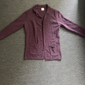 Vinröd cardigan jacka John Henric - Säljer en vinröd cardigan jacka från John Henric. Jackan har två stora fickor framtill, knäppning med tre knappar och en mjuk, stickad struktur. Perfekt för lager-på-lager och enkel att styla till olika outfits.