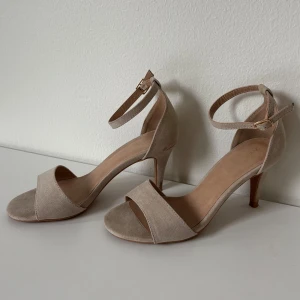 Beiga klackar från Anna Field - Säljer nu dessa snygga klackar från Anna Field (köpta på Zalando). Storlek 38 och normala i storleken. Perfekta till bal eller andra fina tillställningar! Använda en gång. Dessa har ca 8 cm smal klack och ett spänne med olika storleksalternativ runt ankeln. 