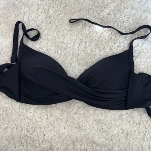 Svart bikiniöverdel med omlott - Säljer en svart bikiniöverdel med omlottdesign och knyt i nacken samt i ryggen🩷