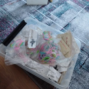 Stort paket med smycken och accessoarer - Säljer en stor plastlåda fylld med olika smycken och accessoarer. Innehåller bland annat färgglada armband, halsband med kors och flera silvriga kedjor. Perfekt för dig som gillar att mixa och matcha olika stilar.