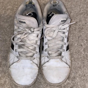 Vita Adidas sneakers med svarta detaljer - Klassiska vita Adidas sneakers med svarta ränder på sidorna och vit sula. Skorna har snörning och rund tå, perfekt för en avslappnad stil. Adidas-logga syns på plösen. Dåligt skick 😭🙏🏻