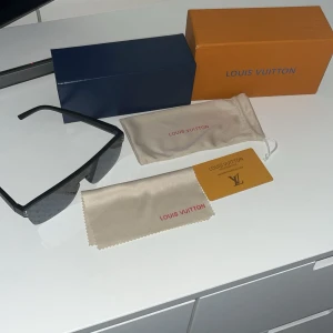 Svarta solglasögon från Louis Vuitton - Snygga svarta solglasögon från Louis Vuitton med monogrammönster på glaset. Modellen har en modern, oversized sköldform och svarta bågar. Perfekt accessoar för dig som vill sticka ut med exklusiv design.