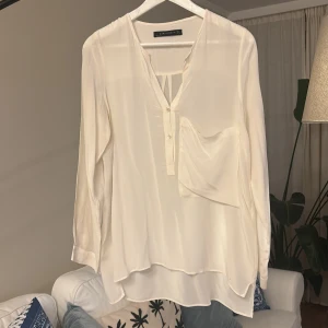 Fin och luftig vit blus med ficka från Zara  - En luftig och vacker blus som lägger sig lätt på kroppen. Dessutom har den en fin ficka på vänster bröst. Storlek S