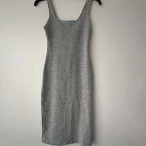 Grå  klänning - Säljer en enkel och stilren grå  klänning med smala axelband och tight passform. 